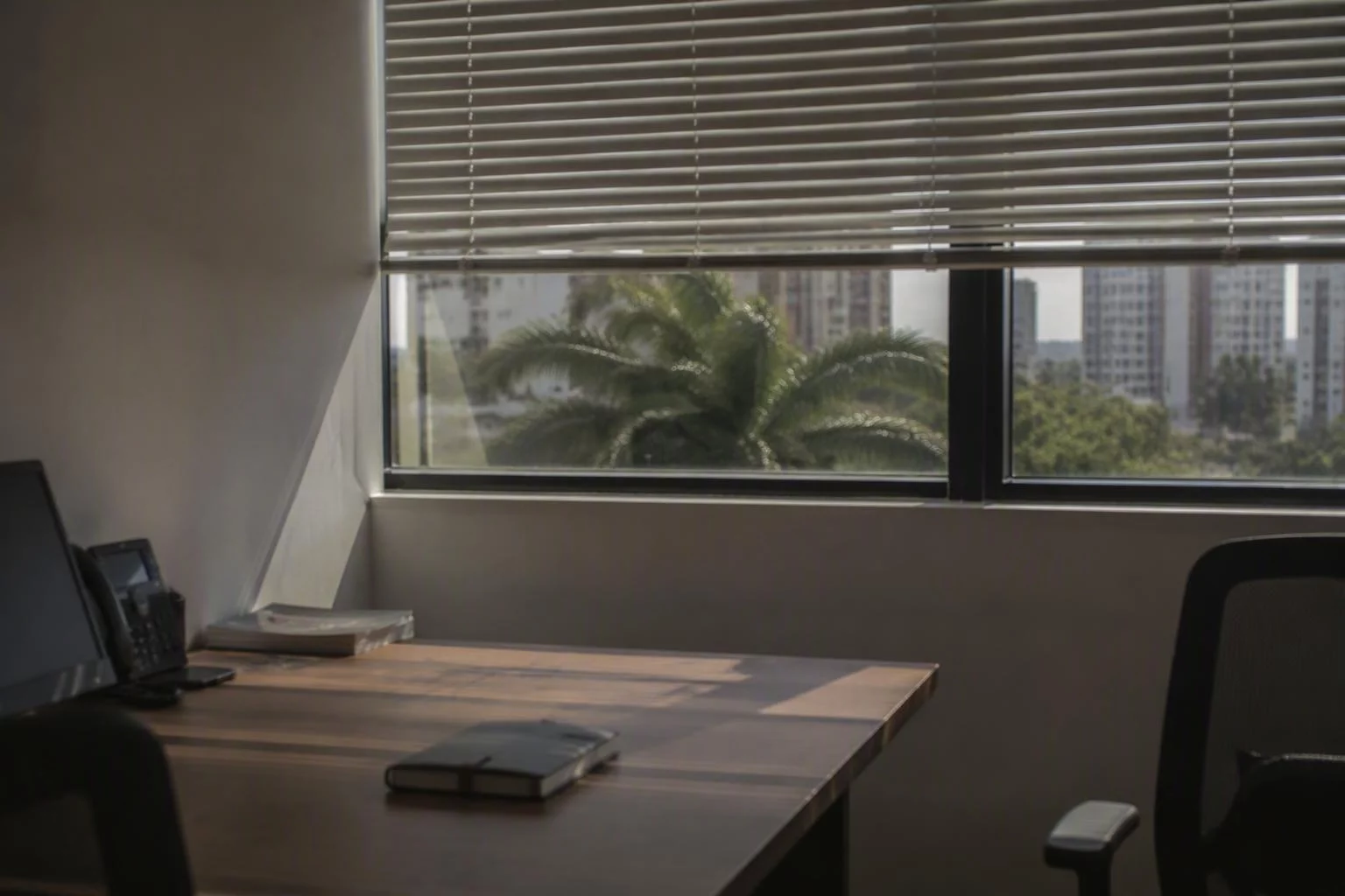 Janela larga com persiana entreaberta sobre a mesa de trabalho